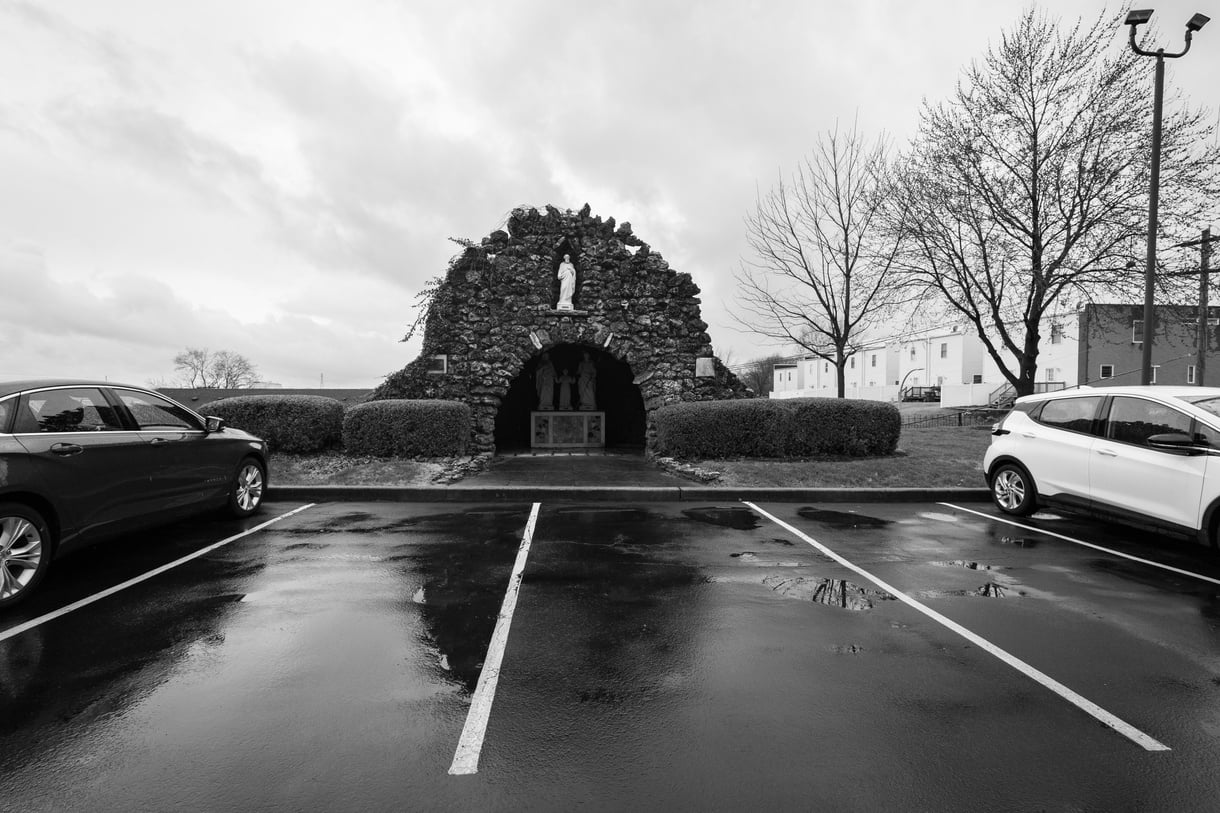 a black and white photo of two cars parked next to a shrine in a parking lot