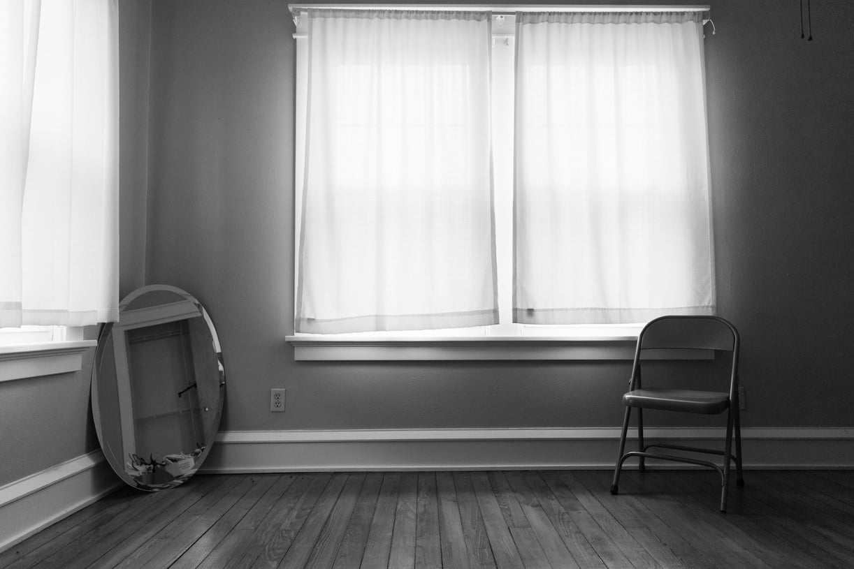 a black and white photo of an empty room with a folding chair and mirror