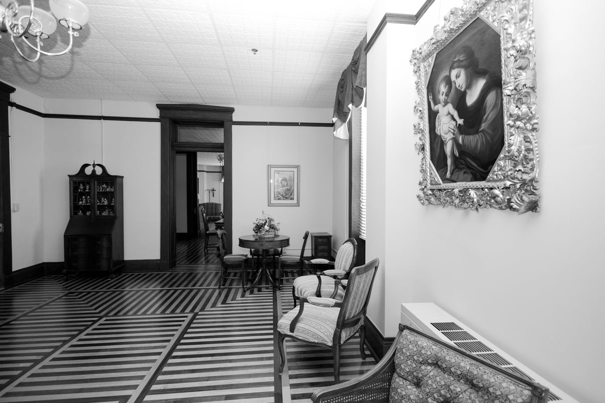 a black and white photo of a living space with a painting of Mary on the wall